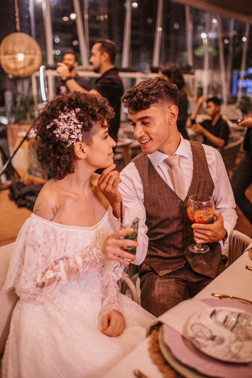 Casal à mesa com taças, sob a luz quente da festa